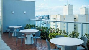 Una terraza en la azotea con mesas y sillas redondas, una cubierta de madera y vistas a la ciudad.