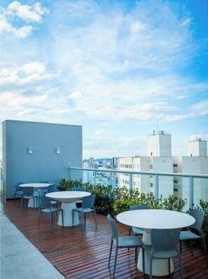 A rooftop terrace with round tables and chairs, a wooden deck, and a cityscape view. - View, Air Conditioning, and Parking Space in the City Center | LYVVO (Campinas)