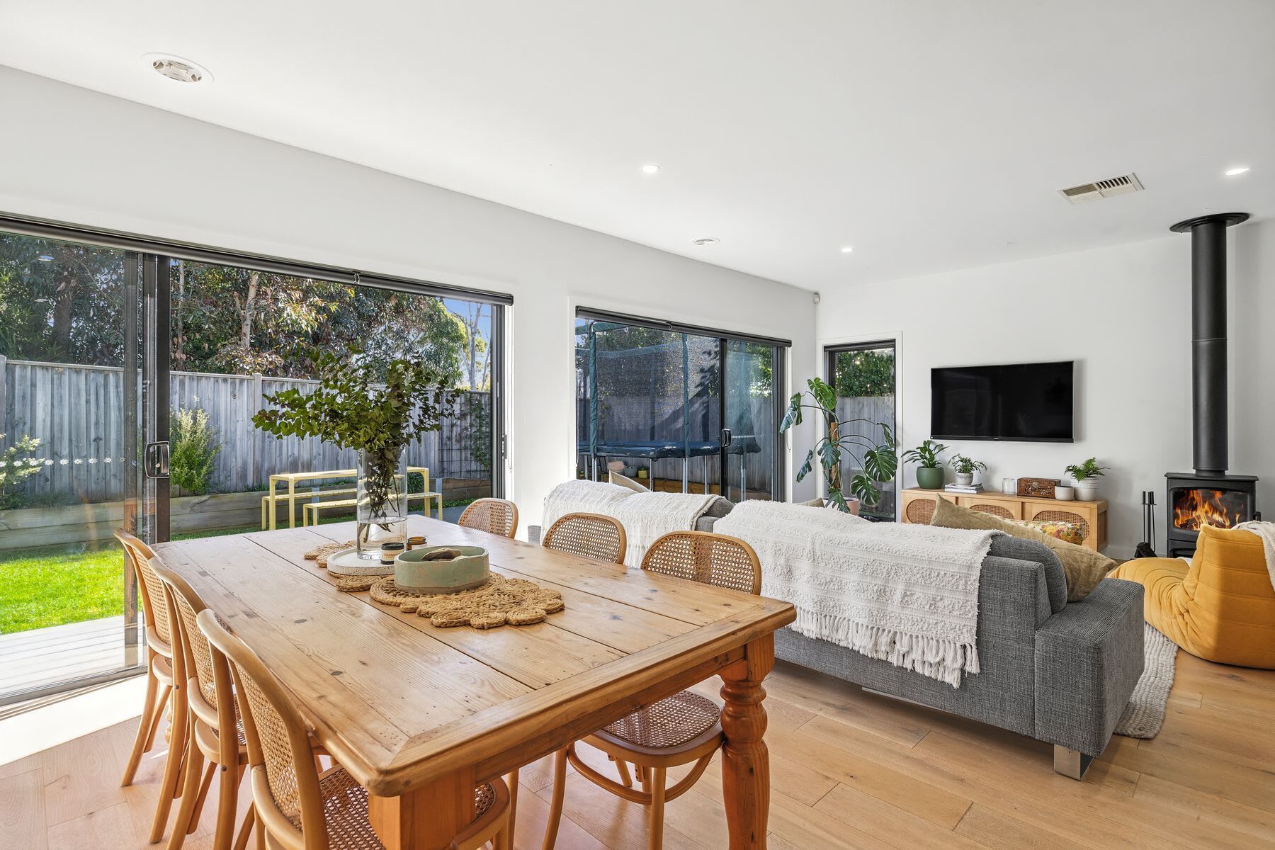 A spacious living area with a wooden dining table, comfortable seating, a fireplace, and large windows offering a view of the outdoors.