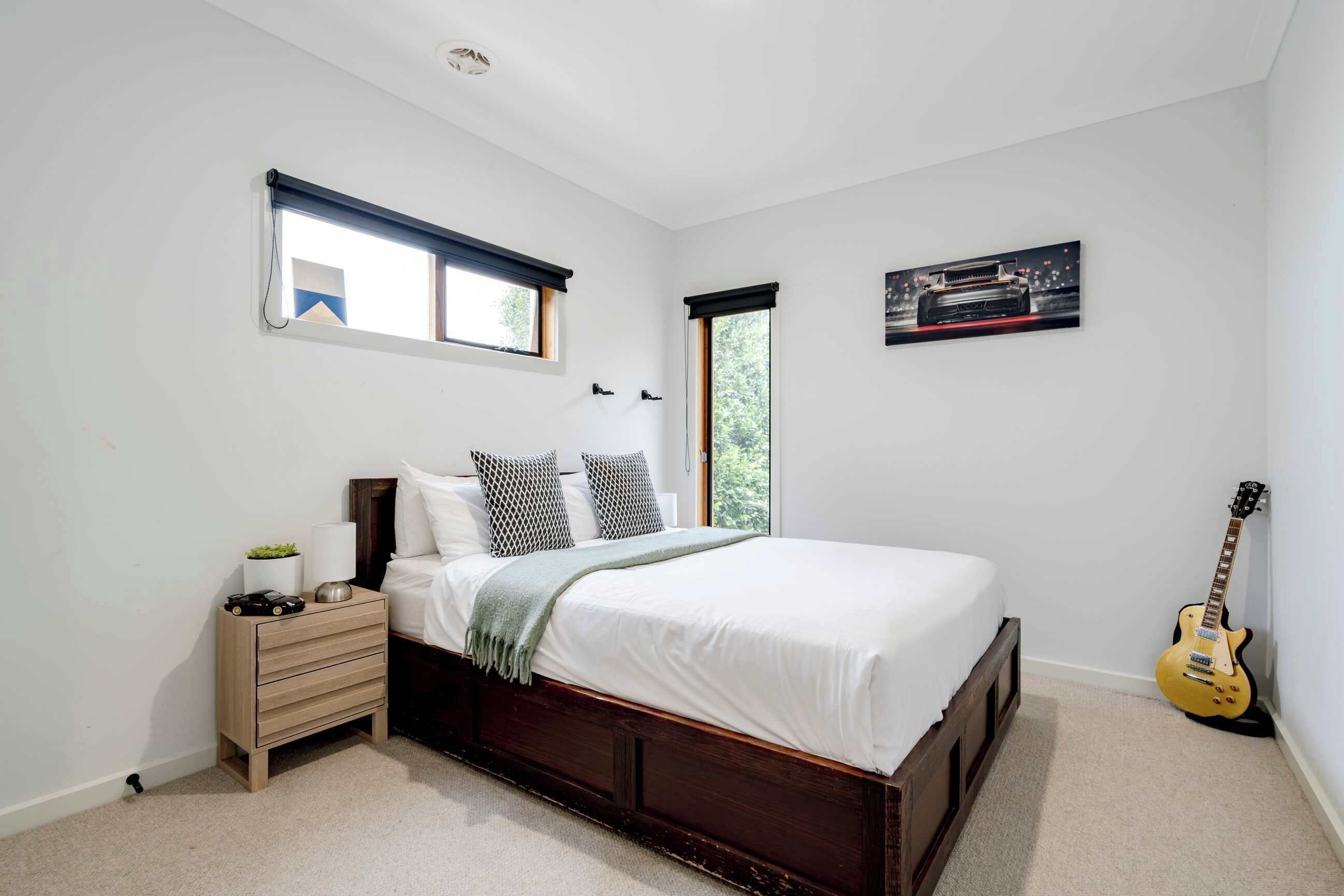 A bedroom with a bed, bedside tables, a nightstand, a window, and a guitar.