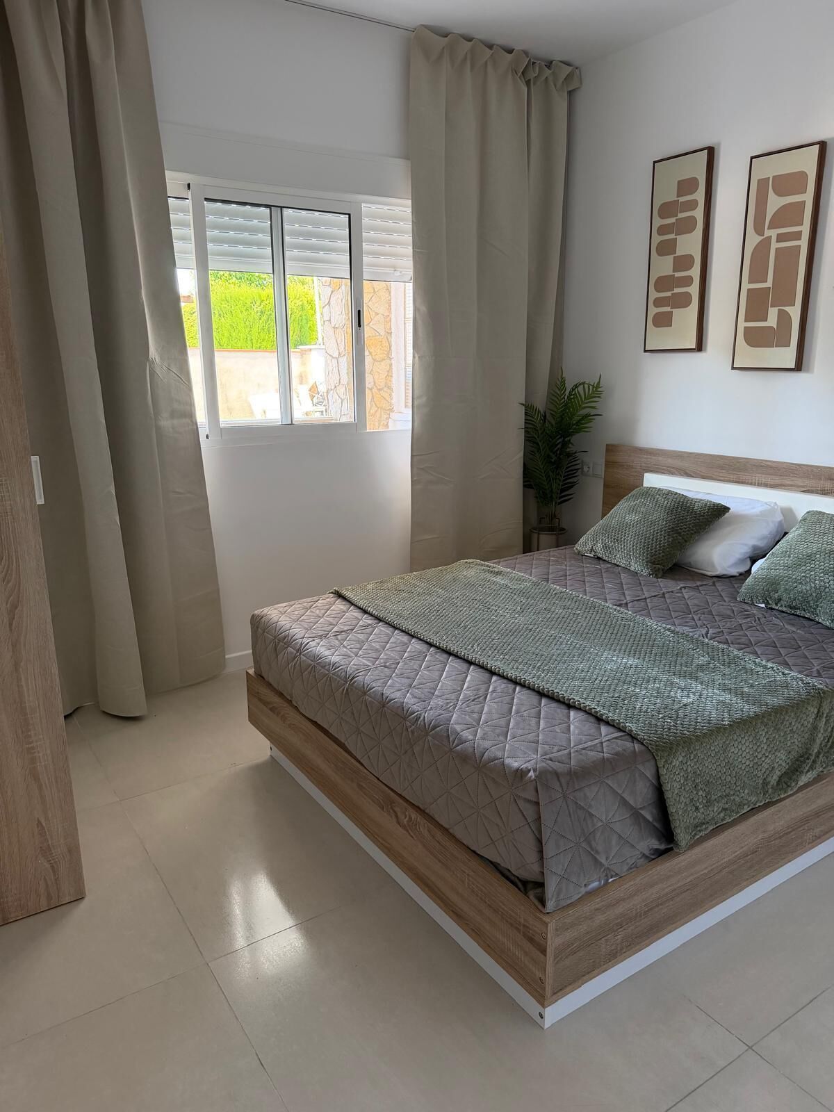 Une chambre à coucher avec un lit, des rideaux, une fenêtre et deux tableaux encadrés accrochés au mur.