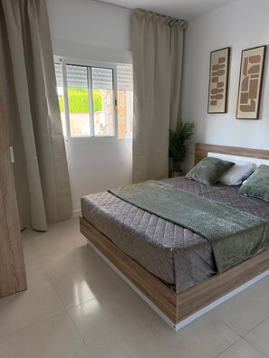 Ein Schlafzimmer mit Bett, Vorhängen, einem Fenster und zwei gerahmten Bildern an der Wand.