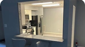 A kitchen with a bar area, two bar stools, a refrigerator, and a microwave. - House in Houston (Houston)