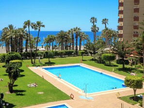 Ein Swimmingpool mit Blick auf das Meer, umgeben von Palmen und einem Gebäude.