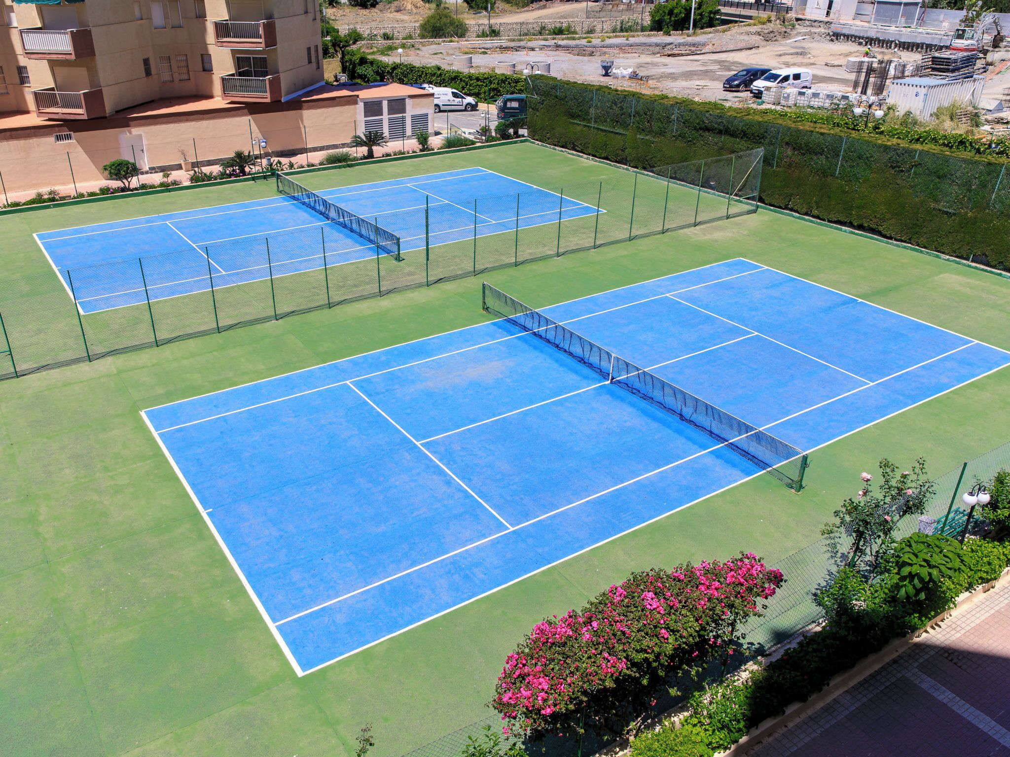 Two tennis courts with surrounding greenery and a residential building in the background.