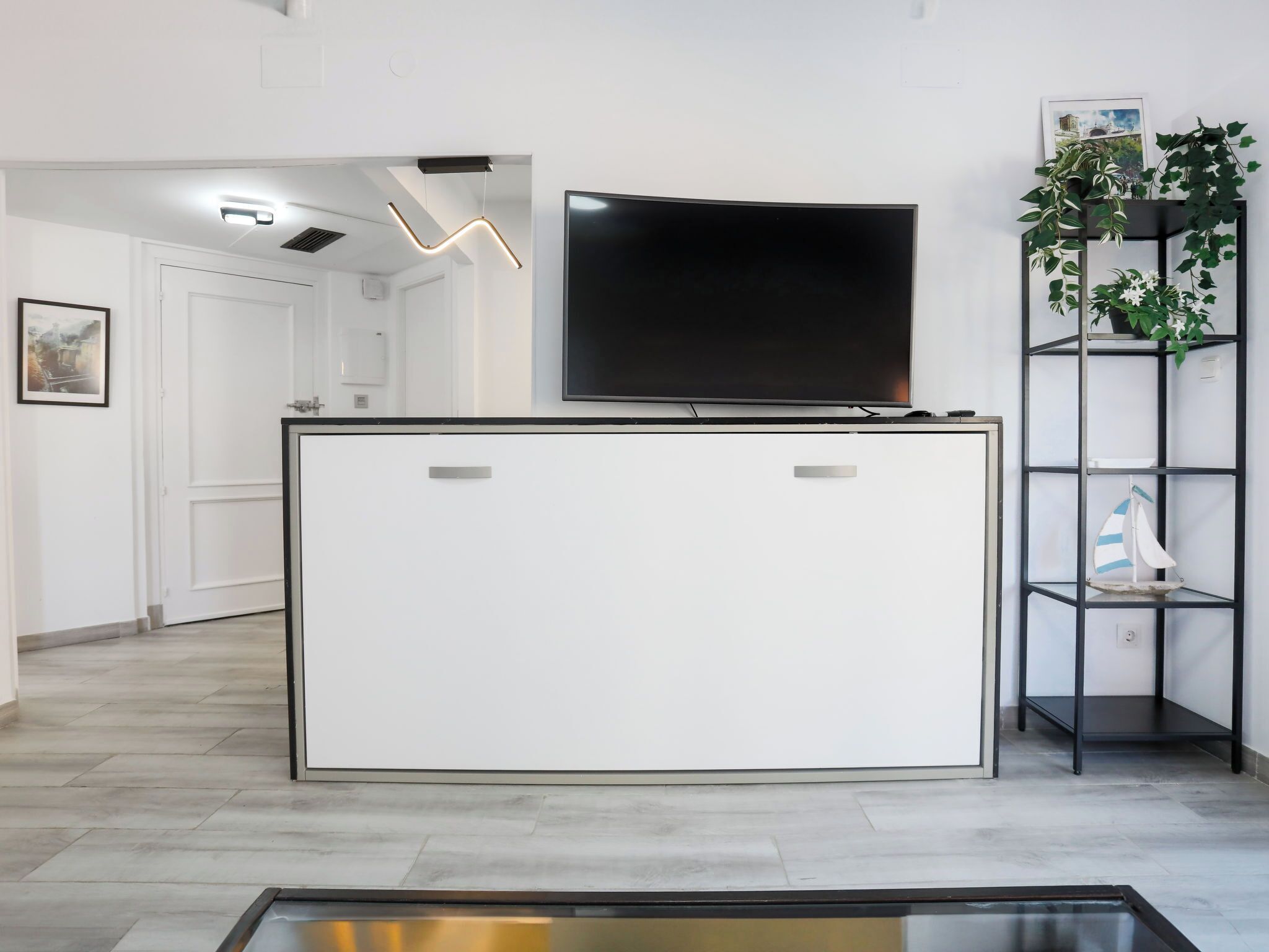 A modern reception area with a flat-screen TV, a white reception desk, and a plant on a black shelving unit.