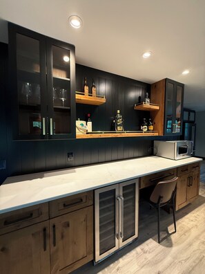 A modern kitchen with dark cabinetry, wooden shelves, and a marble countertop.