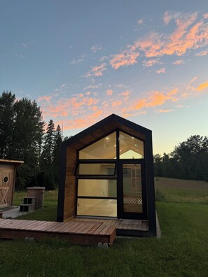 A modern, single-story building with large glass windows and a wooden exterior, situated in a grassy area with trees in the background. - Lonestar Lodge — Private Montana Retreat with Chef's Kitchen, Gym & Hot Tub (Columbia Falls)