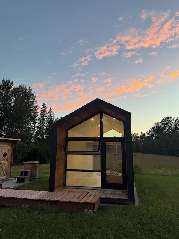 Un bâtiment moderne, de plain-pied, doté de grandes fenêtres en verre et d’une façade en bois, situé dans un espace verdoyant, avec des arbres en arrière-plan.