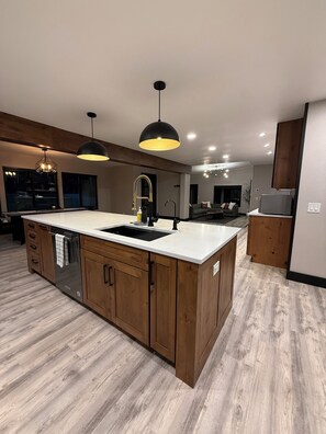 A modern kitchen with a central island, wooden cabinets, and pendant lighting.