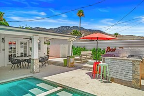 A pool area with a barbecue station, outdoor seating, and a mountain view.