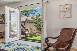 An open sliding glass door leading to a patio with a chair, a small table, and a decorative rug. - Resort-Style Desert Retreat with Huge Pool, Spa city id 069562 City ID # 069562 (Palm Springs)