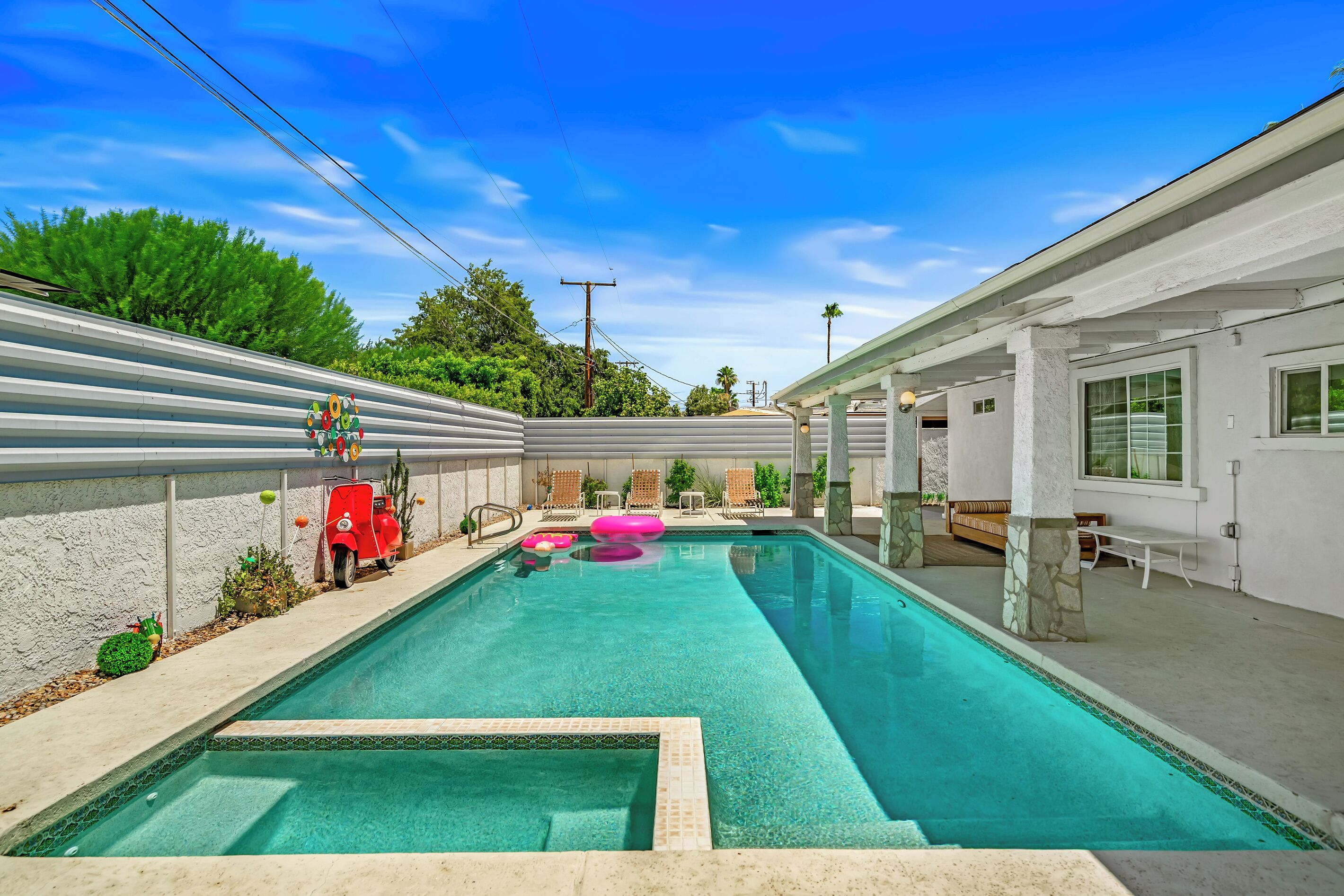 A swimming pool with a stone border, lounge chairs, and a patio area.