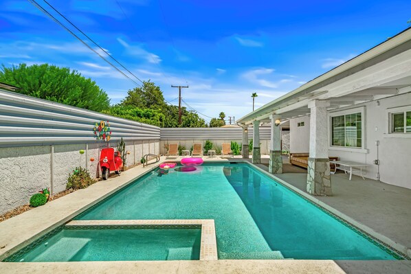 A swimming pool with a stone border, lounge chairs, and a patio area.