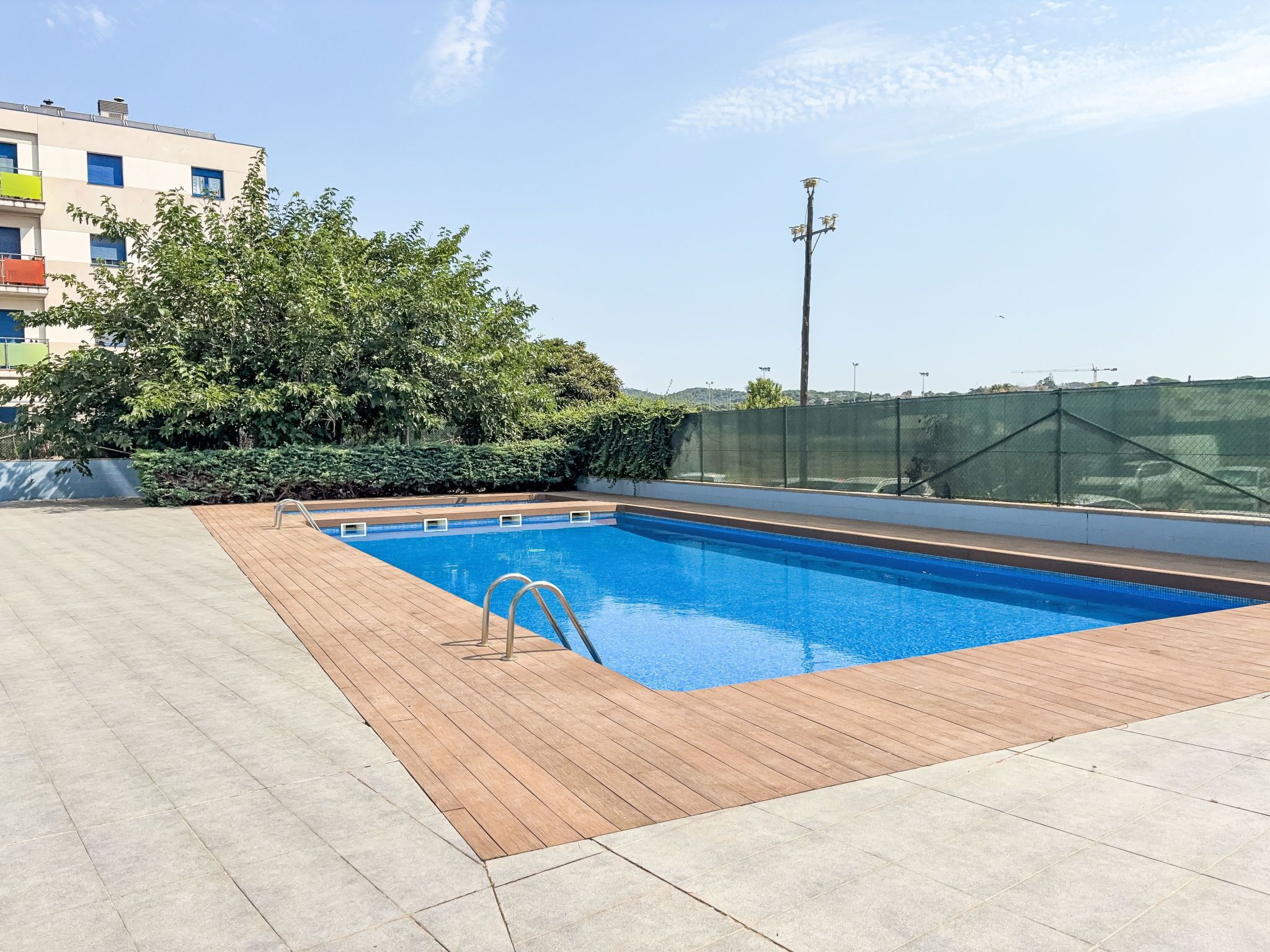Une piscine sur le toit, dotée d’une terrasse en bois, entourée de verdure et offrant une vue sur le paysage urbain.