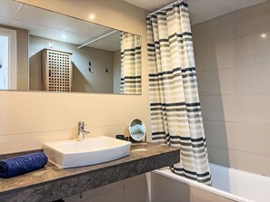 A bathroom with a white sink, a mirror, and a striped shower curtain. - Sonnige Ferien by Interhome (St Antoni de Calonge)