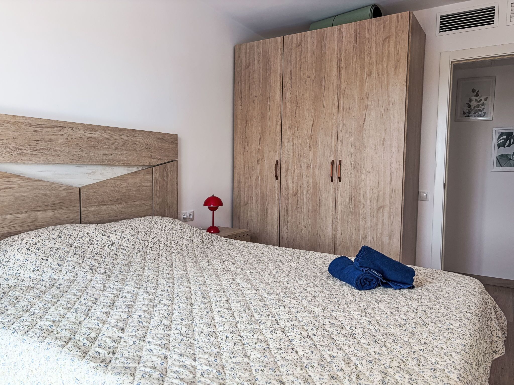 A bedroom with a bed, a wardrobe, a nightstand, and a red lamp.