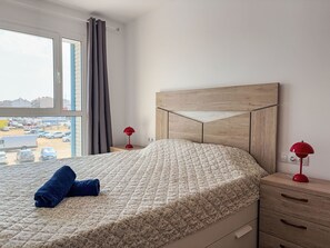 A hotel room with a bed, a window with curtains, a view of a parking lot, and a nightstand with a lamp. - Sonnige Ferien by Interhome (St Antoni de Calonge)