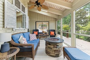 A covered outdoor seating area with wicker furniture, a stone fire pit, and a view of a bedroom through a glass door.