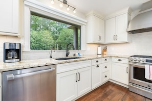 A modern kitchen with white cabinets, a stainless steel dishwasher, a coffee maker, a sink with a curved faucet, and a stove. - Lakefront 3-bedroom house on Poe Creek at Lake Gaston. Bring your boat! (Littleton)