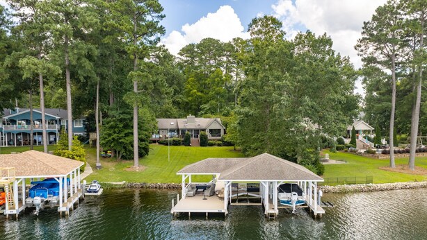 A lakeside property with a dock, a covered seating area, and a house in the background. - Lakefront 3-bedroom house on Poe Creek at Lake Gaston. Bring your boat! (Littleton)
