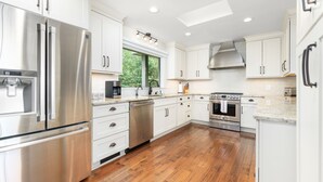 A modern kitchen with stainless steel appliances, white cabinetry, and a wooden floor. - Lakefront 3-bedroom house on Poe Creek at Lake Gaston. Bring your boat! (Littleton)