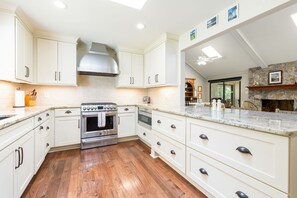A kitchen with white cabinets, a stainless steel range, and a stone fireplace.