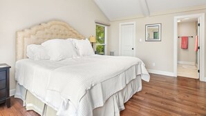 A bedroom with a large bed, a nightstand, a window, and a door leading to another room. - Lakefront 3-bedroom house on Poe Creek at Lake Gaston. Bring your boat! (Littleton)