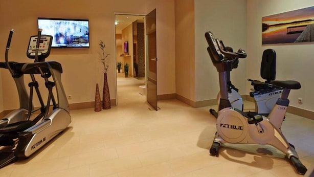 Ein Heimfitnessraum mit zwei Fahrradergometer, einem Fernseher und einem Flur, der in einen anderen Raum führt.