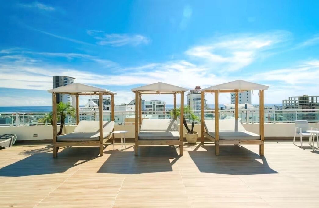 A rooftop terrace with three wooden gazebos, each with a cushioned seat and a potted plant.