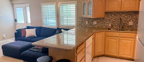 A modern kitchen with a built-in island, wooden cabinets, and a large window with blinds.