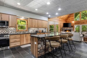 A modern kitchen with a stone island, wooden cabinets, and a stone fireplace. - Private Luxury Cabin | Hot Tub | Sauna | Sleeps 13 (Blue Ridge)
