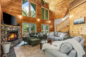 A log cabin interior with a stone fireplace, multiple seating areas, and a staircase. - Private Luxury Cabin | Hot Tub | Sauna | Sleeps 13 (Blue Ridge)