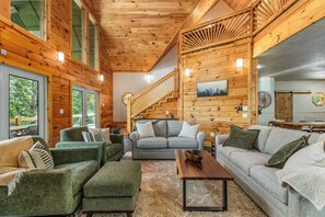A log cabin interior with a staircase, two sofas, a coffee table, and a dining area. - Private Luxury Cabin | Hot Tub | Sauna | Sleeps 13 (Blue Ridge)