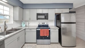 A modern kitchen with grey cabinets, a stainless steel refrigerator, a microwave, and an oven. - Chic & Cozy Home, Perfect for Work + Weekend stays, Near Main Highways (Houston)