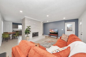 A modern living room with a fireplace, a dining area, and a kitchen in the background. - Chic & Cozy Home, Perfect for Work + Weekend stays, Near Main Highways (Houston)