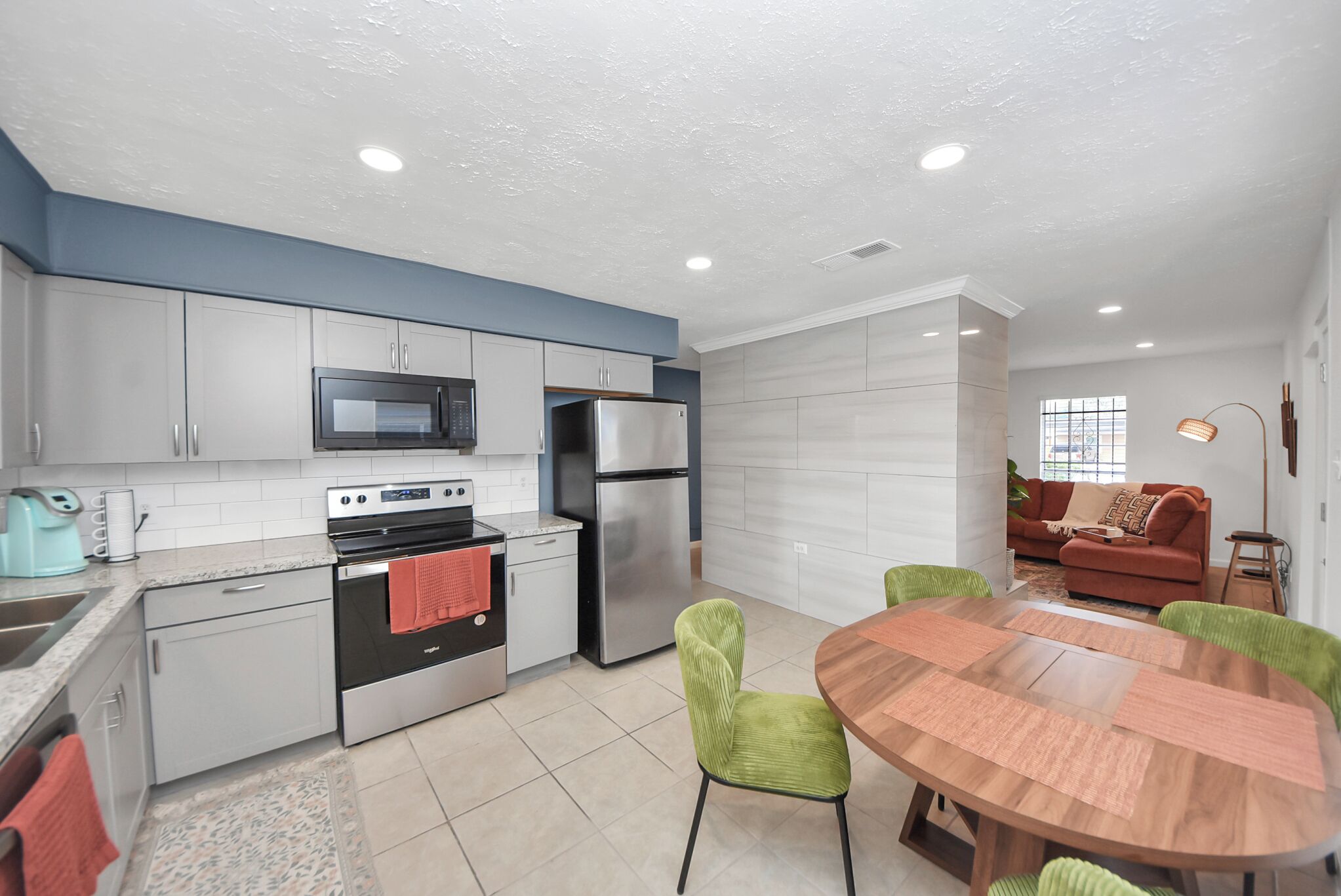 A modern kitchen with a microwave, oven, and refrigerator. There is a dining area with a round table and chairs.
