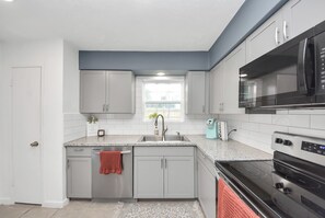 A modern kitchen with grey cabinets, a stainless steel sink, a microwave, and an oven. - Chic & Cozy Home, Perfect for Work + Weekend stays, Near Main Highways (Houston)