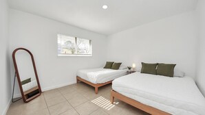 A bedroom with two beds, a window with blinds, a bedside table with a lamp, and a mirror. - Chic & Cozy Home, Perfect for Work + Weekend stays, Near Main Highways (Houston)