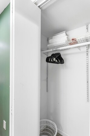 Ein weißer Kleiderschrank mit Regalen, einer Kleiderstange und einem Wäschekorb.