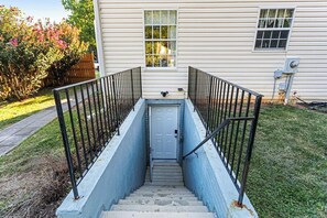 Una casa con una escalera delantera que lleva a una puerta, rodeada por un patio cercado y un seto.