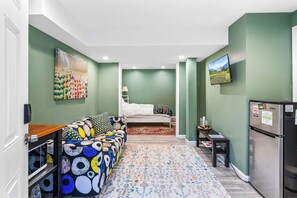 A compact living space with a sofa, a bed, a small table, and a refrigerator. - Cozy 2-bedroom house in peaceful Woodbridge with AC (Woodbridge)