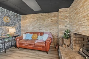 Una sala de estar acogedora con pared de ladrillo, un sofá de cuero, una chimenea y un reloj de pared.