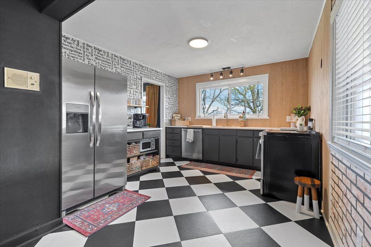 Una cocina con piso blanco y negro a cuadros, refrigerador de acero inoxidable y gabinetes de madera.