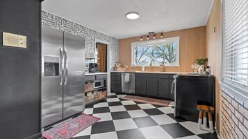 Una cocina con piso blanco y negro a cuadros, refrigerador de acero inoxidable y gabinetes de madera.