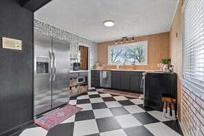 Una cocina con piso blanco y negro a cuadros, refrigerador de acero inoxidable y gabinetes de madera.