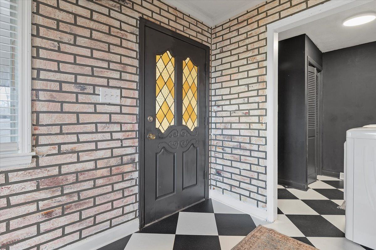 Una puerta negra con un panel de vidrio con diseño de rombos, un muro de ladrillo y un suelo a cuadros.