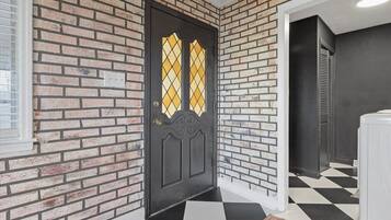 Una puerta negra con un panel de vidrio con diseño de rombos, un muro de ladrillo y un suelo a cuadros.