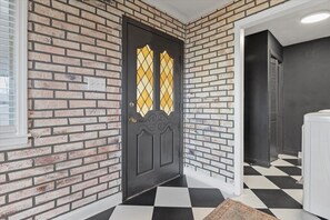 Una puerta negra con un panel de vidrio con diseño de rombos, un muro de ladrillo y un suelo a cuadros.