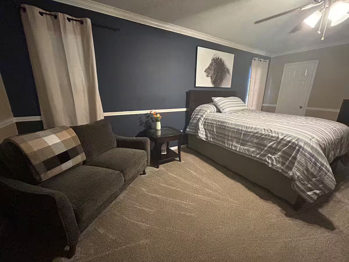 A bedroom with a bed, a sofa, a nightstand, and a ceiling fan.